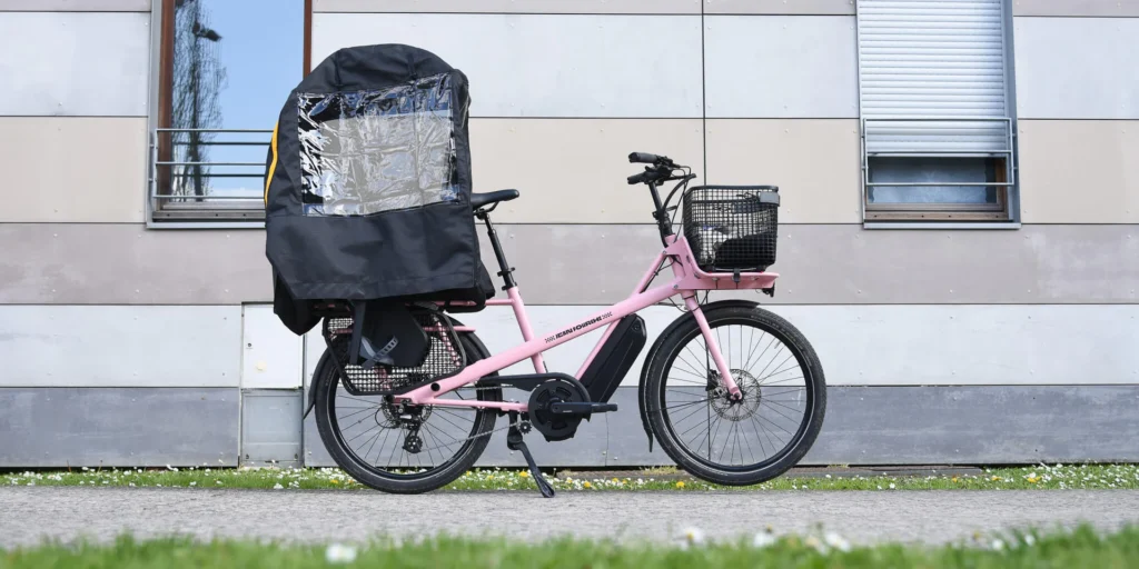 Vélo Jean Fourche équipé de la protection pluie Decathlon transportant deux enfants par temps pluvieux