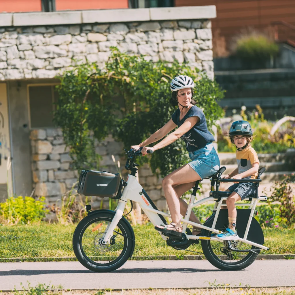Vélo cargo shortail Yuba Mini Boda Boda bleu avec passager sur le porte-bagages arrière équipé de Monkey Bars