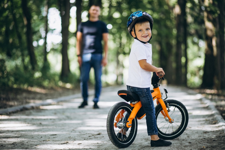 Père qui apprend à son enfant à faire du vélo dans un parc - guide taille vélo enfant