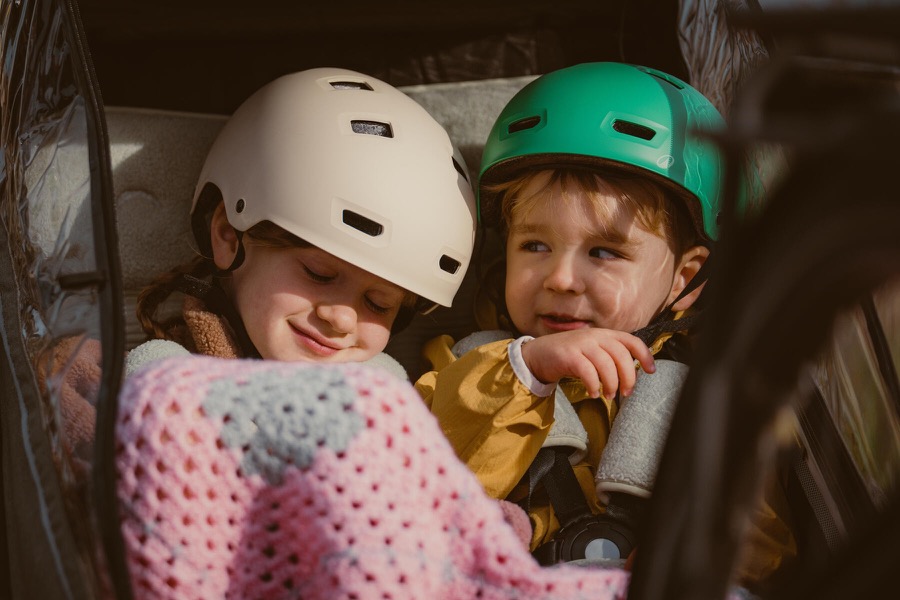 Gros plan sur deux enfants casqués blottis sous une couverture dans la cabine d'une remorque vélo enfant