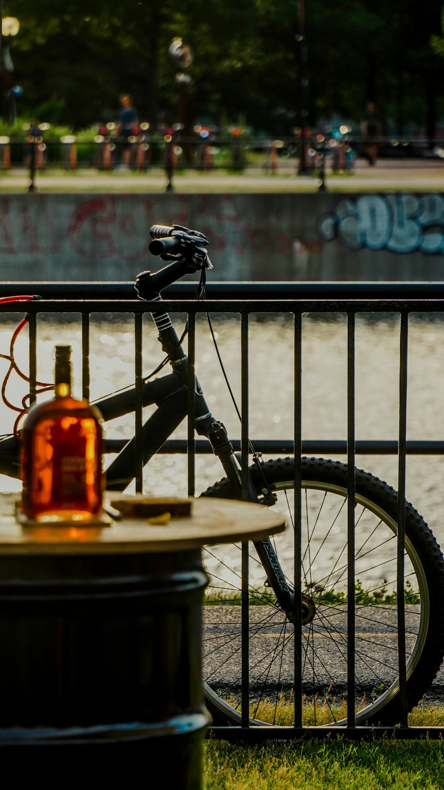 Bouteille d'alcool posée à côté d'un vélo au bord de l'eau au coucher du soleil