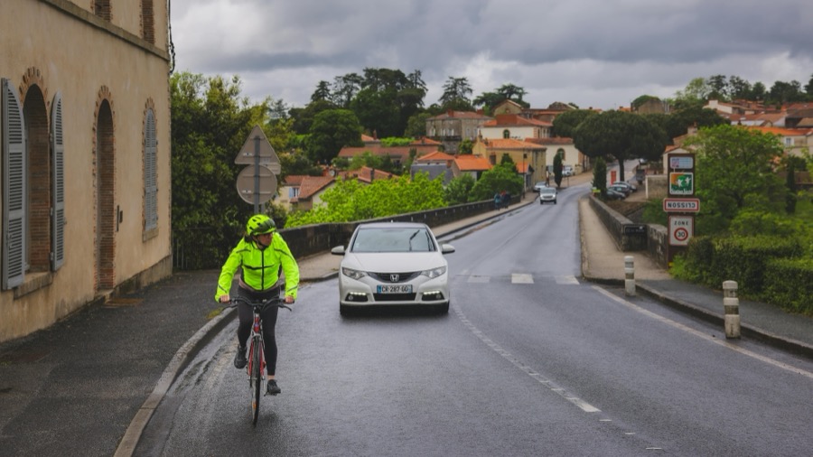 Cycliste roulant sur la chaussée suivi d'une voiture en ville