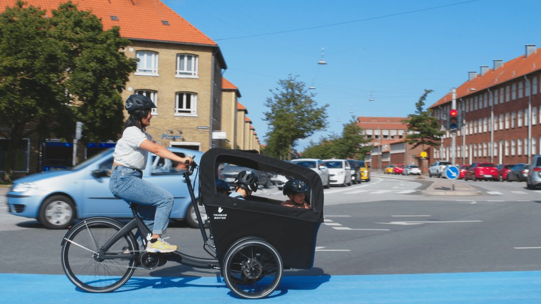 Triobike Boxter conduit en ville avec deux enfants à bord
