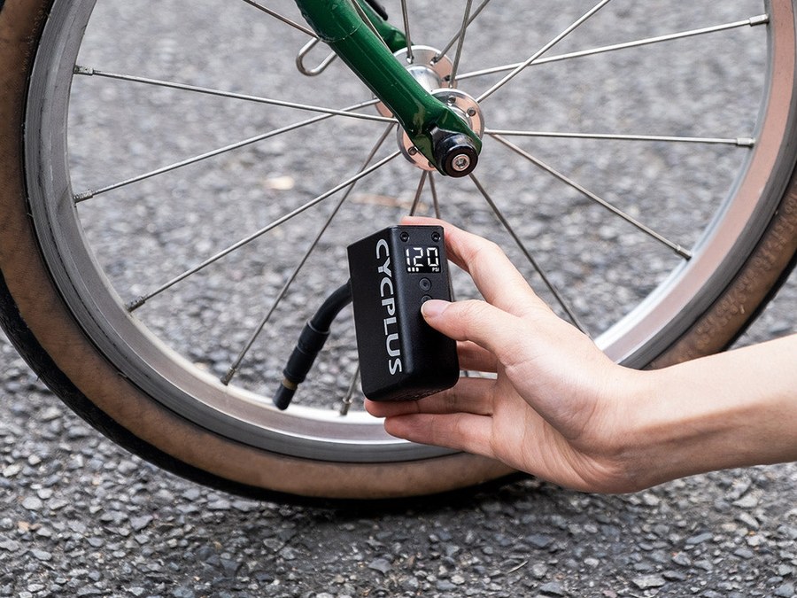 Main tenant la pompe électrique CYCPLUS AS2 Pro branchée sur la valve d'une roue de vélo avec son flexible de rallonge