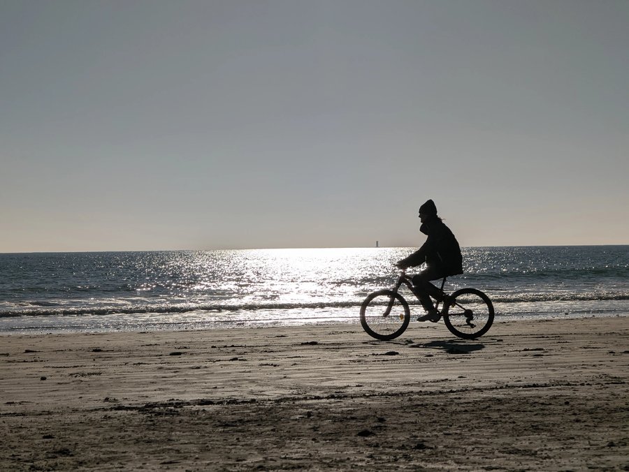 Cycliste en contre-jour sur le sable humide, face à la mer et au soleil