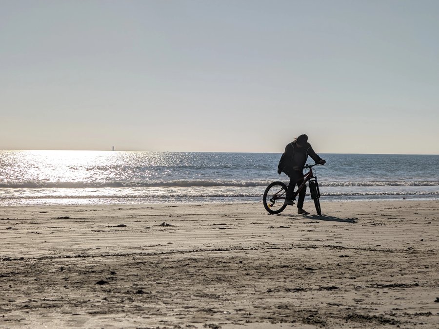 Cycliste à l'arrêt, pied à terre sur le sable d'une plage, face à la mer